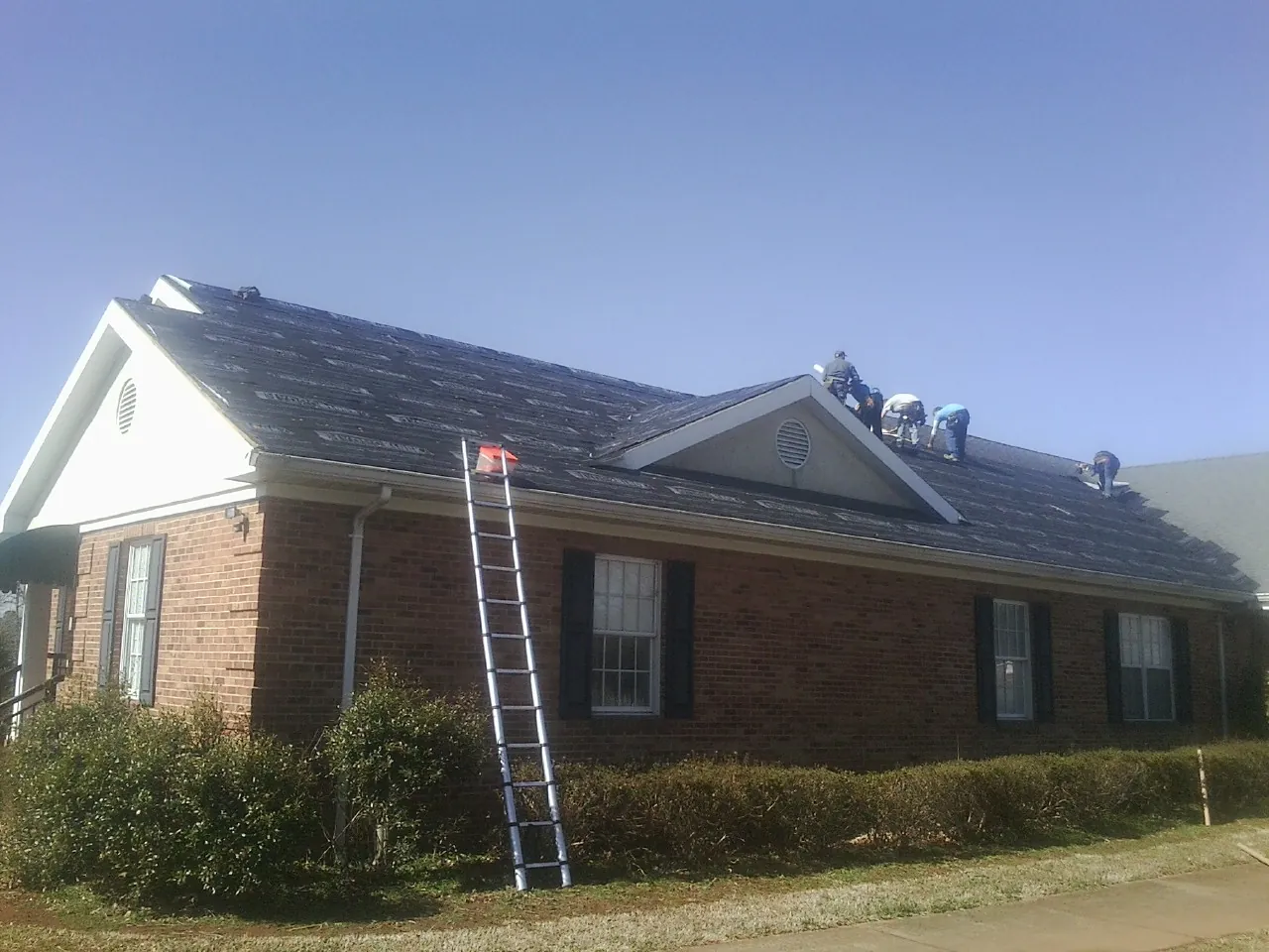 Crew tearing shingles off a brick ranch roof with a ladder set — Emergency Roof Repair work by our crew in Kenmare