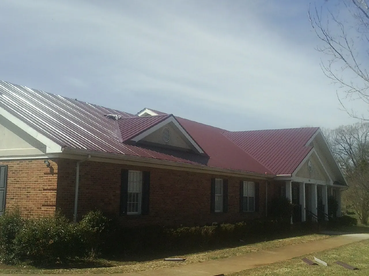 Red metal roof with gabled entries on a long brick building, from a Hail Damage Roof Repair job in Kenmare