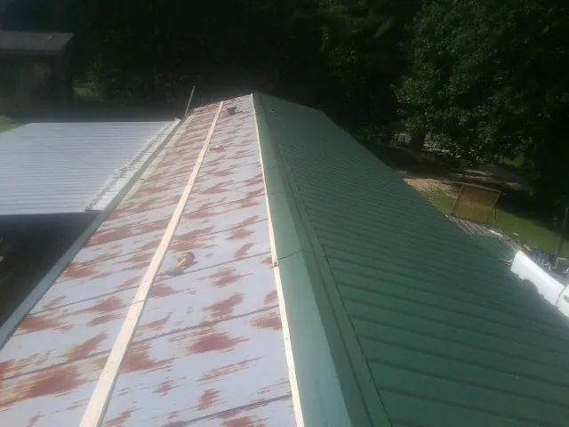 Old rusted panels beside newly installed green metal roofing — Wind Damage Roof Repair by Roofing Brothers in Kenmare