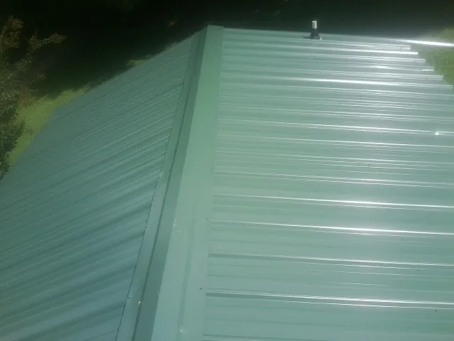 New green metal panels meeting at the ridge of a roof — Flat Roof Repair work by our crew in Kenmare
