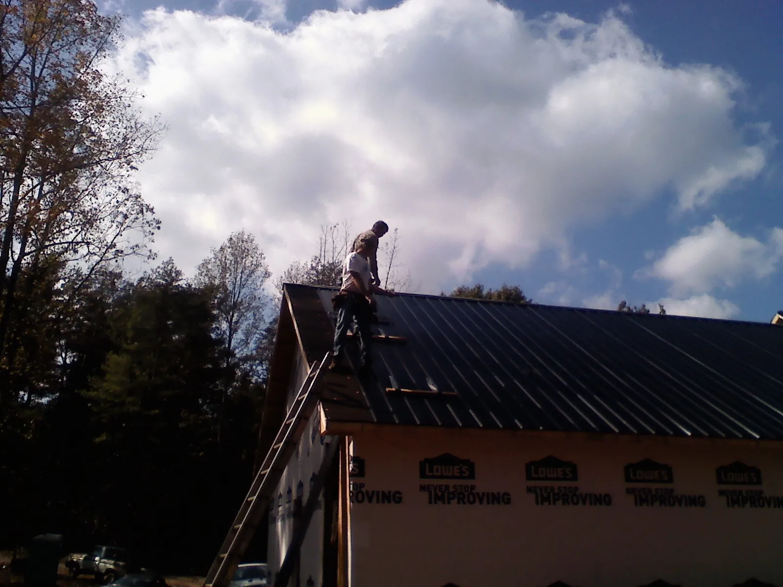 Roofer fastening dark metal panels high against a cloudy sky, from a Roof Inspection job in Kenmare