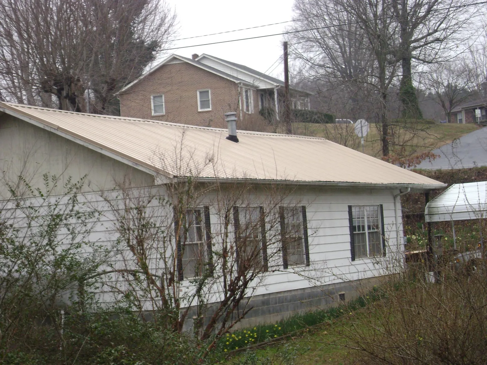 Tan metal roof on a white sided house set into a hillside — Commercial Roofing by Roofing Brothers in Kenmare